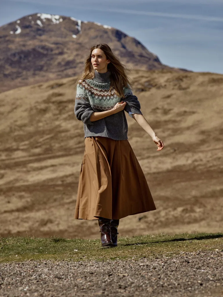 Frau in Norwegerpullover und camelfarbenem Rock in einer Heidelandschaft