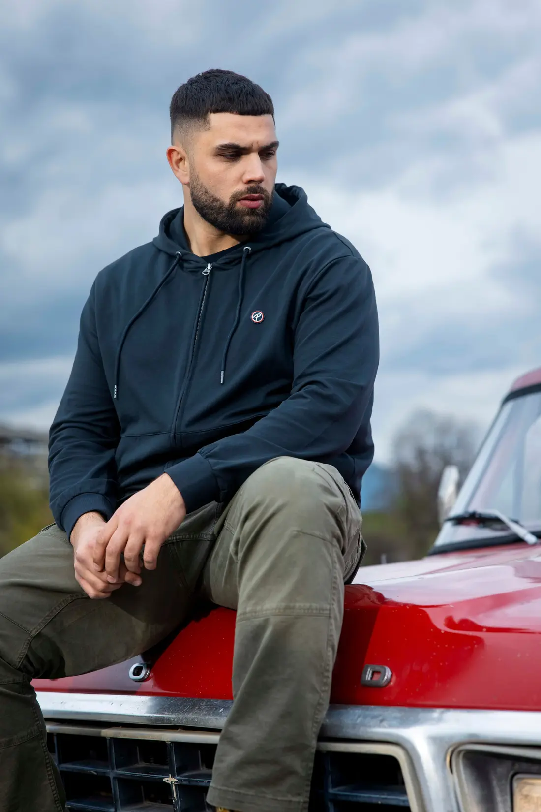 Mann im dunkelblauen Hoodie sitzt auf der Front eines roten Autos
